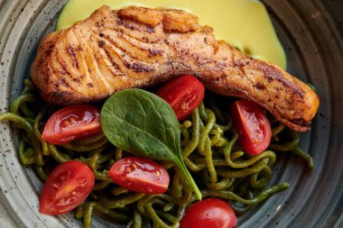 Yeşil pici makarnalı somon bifteği, vintage tabakta kiraz domates ve peynir sosu. Restoranda kırmızı balıklı sağlıklı bir yemek. - Yakın çekim. Akdeniz mutfağı.