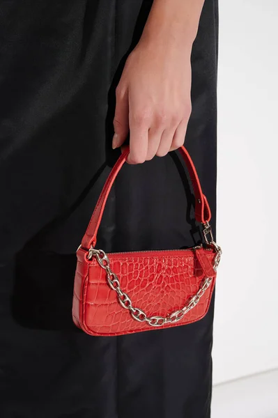Beautiful red leather handbag in girl's hand. Luxury handmade bag against black dress with reptile effect. Fashionable modern accessory. Vertical photo.