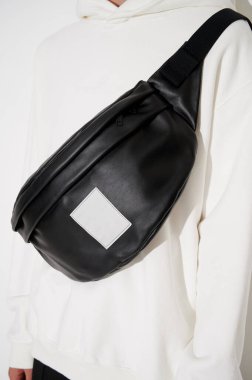 Siyah deri çantalı, beyaz kapüşonlu bir adam. Logo ya da reklam için boş alan. Moda geçmişi. Dikey fotoğraf.