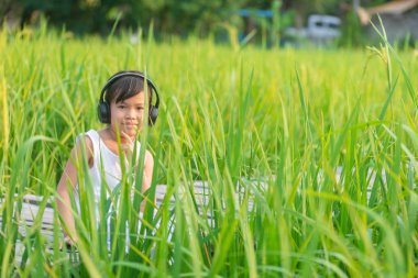Asya sevimli kız oturuyor ve müzik doğa arka plan ile ayarla güneş pirinç alanında ahşap köprü üzerinde rahatlatıcı. Güneş ile doğa arka plan ayarlamak pirinç alanında ahşap köprü '.