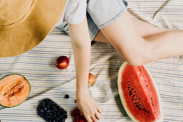 Yaz piknik ayarı. Kadın şort ve şapka eatining karpuz, kavun, böğürtlen, ahududu ve şeftali, içme suyu. Dış toplama kavramı.