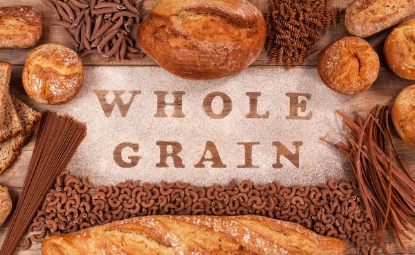 Bakery products and pasta made of whole grains flour framing wholemeal layer on table with text - top view