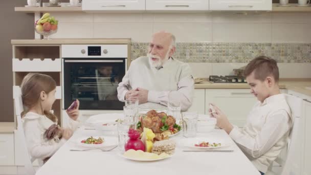 Дедушка общается с внуками за столом перед семейным ужином — стоковое видео