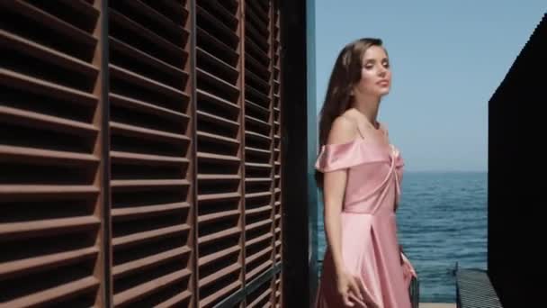 Elegantes Mädchen im Abendkleid posiert an einem glücklichen Sommertag in der Nähe eines Hotelgebäudes am Meer. — Stockvideo