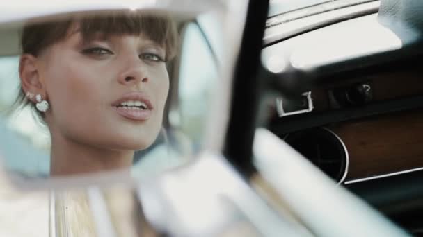 Jeune belle femme en robe de mariée posant dans une voiture vintage . — Video