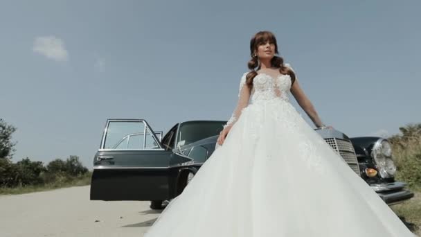 Молодая красивая женщина в свадебном платье позирует возле винтажного автомобиля . — стоковое видео