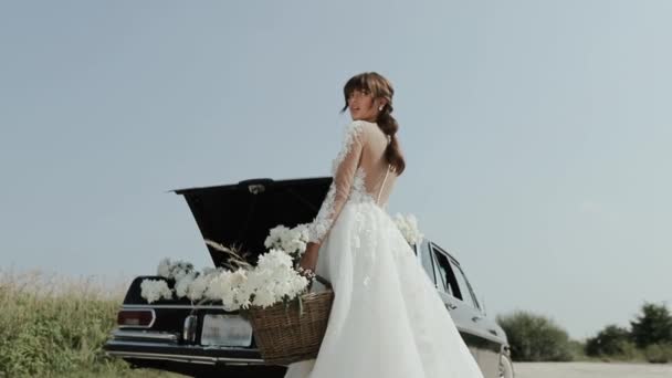 Jovem bela mulher no vestido de casamento posando perto de carro vintage . — Vídeo de Stock