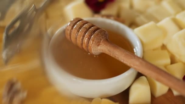 Miel dulce en placa de madera con diferentes quesos, flores y frutos secos . — Vídeos de Stock