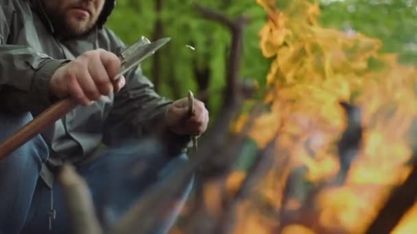 カジュアルな強い男のスローモーションは、野生の落葉林のキャンプで暖かい焚き火の近くで斧と木で動作します. — ストック動画