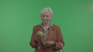 Yaşlı Kadın Yeşil Arka Plan Üzerinde İzole Elinde Elma İnceler.