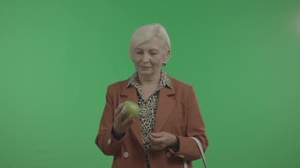 Mujer mayor examina manzana en su mano aislada sobre fondo verde . — Vídeo de stock