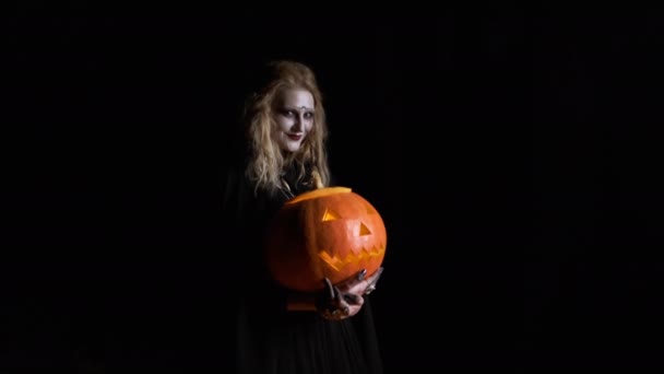 Halloween Afbeelding .Jonge heks in zwarte kleren houdt pompoen in haar handen. — Stockvideo