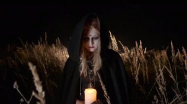 Cadılar Bayramı resmi. Siyah Başlıklı Cadı. Cadı kılığındaki genç sarışın başını eğiyor..