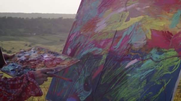 少女は絵を描く。アーティストは丘の上に立って、彼女の手にブラシで風景を見て. — ストック動画