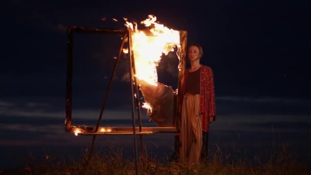 Jeune fille artiste se tient dans la nature au crépuscule devant un chevalet avec une image brûlante. — Video