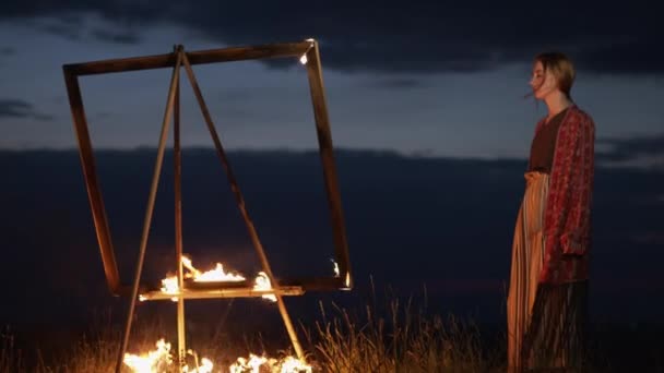 Junge Künstlerin steht in der Dämmerung in der Natur vor einer Staffelei mit brennendem Bild. — Stockvideo