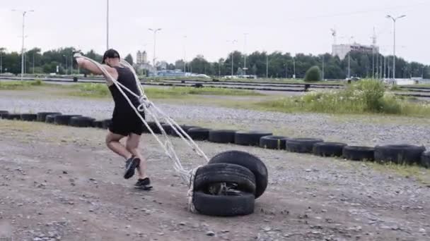 Athletischer Typ macht Sport. Mann rennt und zieht Autoreifen an Seil. — Stockvideo