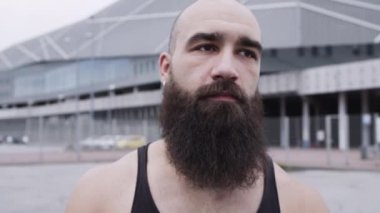 Sakallı genç sporcunun yüzü. Adam sokakta dikiliyor..