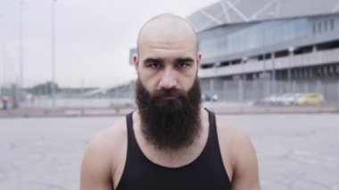 Sakallı genç sporcunun yüzü. Adam sokakta dikiliyor..