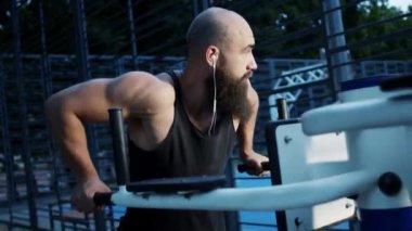 Sakallı ve kulağı delik genç adam spor için geliyor. Spor Simülatörü üzerine çalışıyor..