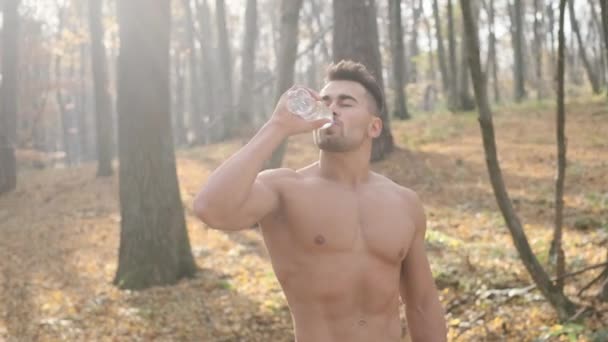 Young Athletic Guy With Naked Torso Stands In The Woods And Drinks Water. — Stock Video