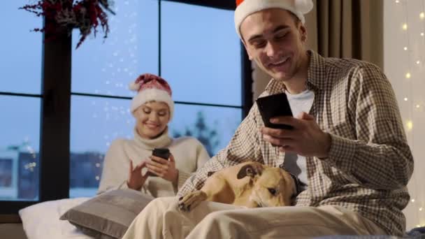 Año Nuevo. joven pareja en santa sombreros en nuevo año víspera en casa con su perro. — Vídeos de Stock