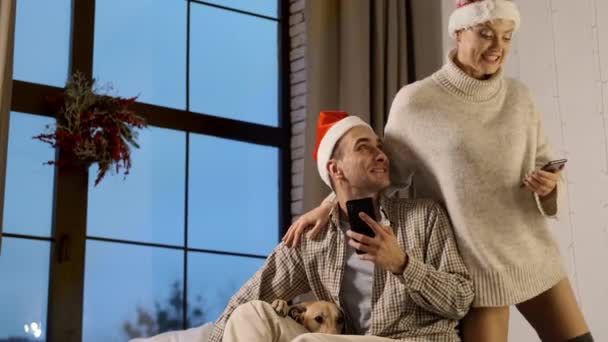 Nouvel An. Jeune couple dans Santa Chapeaux avec téléphones mobiles dans les mains. — Video