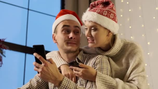 Yeni yıl. Cep telefonlu Noel Baba Şapkalı Genç Çift. — Stok video