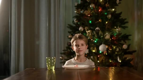 Ano Novo. Engraçado menino sentado na mesa e come a salsicha. — Vídeo de Stock