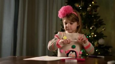 Yeni yıl. Küçük güzel kız masaya oturur ve kağıt parçasına resim çizer..