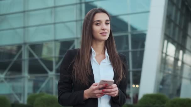 Jonge mooie zakenvrouw lacht. Meisje staat op straat met mobiele telefoon in haar handen — Stockvideo