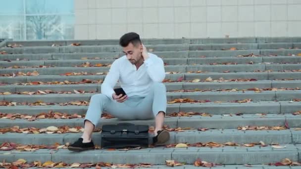 Молодой человек, сидящий на лестнице здания. — стоковое видео