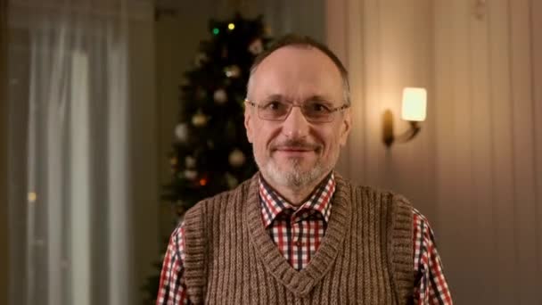 Um homem idoso está em um apartamento no fundo da árvore de Natal. Ano Novo — Vídeo de Stock