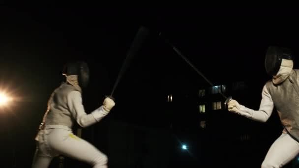 Twee Fencers in Schermpakken en Helmen Schermen in het donker buiten — Stockvideo