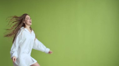 Uzun saçlı kız açık yeşil duvarın arkasında dans ediyor..