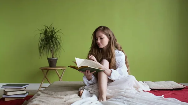 Jente som sitter på sengen og leser i boka. – stockfoto