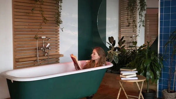 Tyttö istuu kylpyammeessa ilman vettä ja lukemat kirja. tekijänoikeusvapaita kuvapankkikuvia
