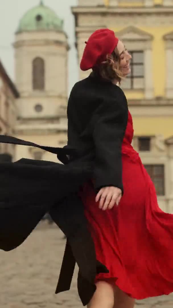 Mosolygó fiatal nő piros sapkában és piros ruha sétál a City Square. — Stock videók