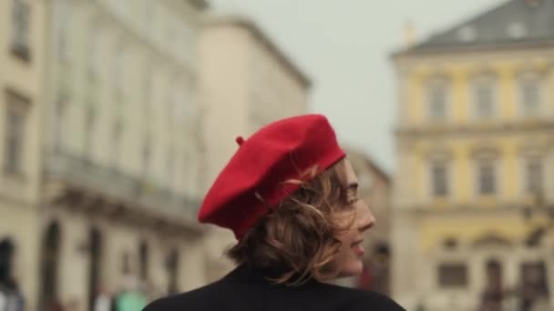 Sorrindo jovem mulher em vermelho boina e vestido vermelho correndo através da praça da cidade. Vídeo De Bancos De Imagens