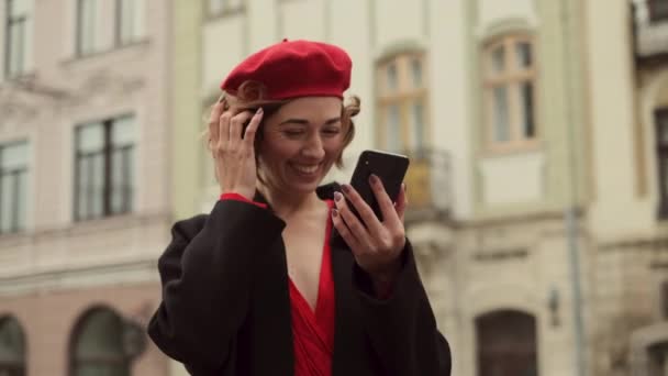 Snygg ung kvinna i rött står i mitten av gatan med mobiltelefon i händerna. — Stockvideo