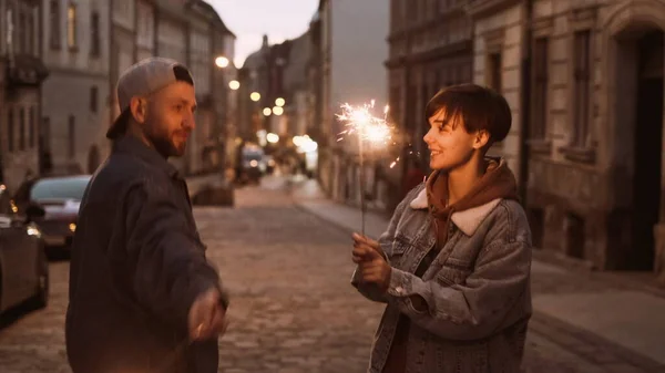 Junges stylisches Paar spaziert durch die City Street. In ihren Händen die brennenden Wunderkerzen. — Stockfoto