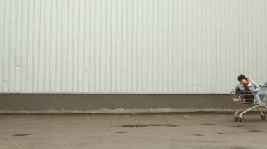 Sokaktaki genç adam içinde kız olan alışveriş arabasını itiyor..