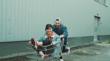 Sokaktaki genç adam içinde kız olan alışveriş arabasını itiyor..