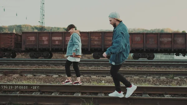 Guy And The Girl Go On The Parallel Rails Of The Railway Track (en inglés). Tratan de mantener su equilibrio. Hay tren en la otra vía. —  Fotos de Stock