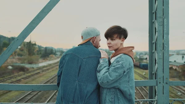 Dater kjæreste og kjæreste på broen. Stilig jente med kort frisyre og en fyr med kappe. – stockfoto