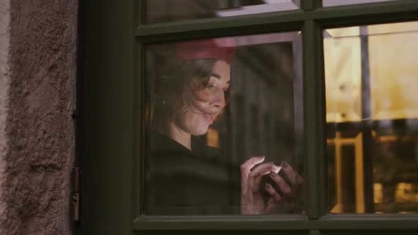 Jovem mulher fora da janela usa telefone celular. Mulher se levanta encostada à janela. — Vídeo de Stock