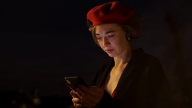 Alacakaranlık. Elinde cep telefonuyla caddenin ortasında dikilen Kırmızılı Şık Genç Kadın.