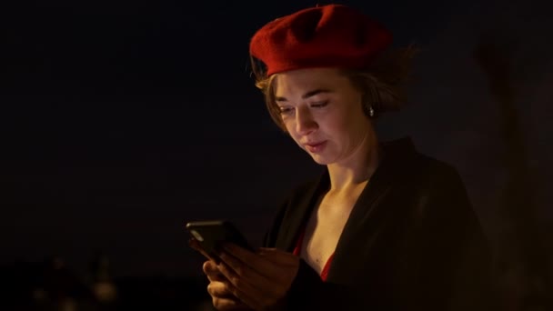 Alkonyat. Stílusos, vörös ruhás fiatal nő áll az utca közepén mobiltelefonnal a kezében.. — Stock videók