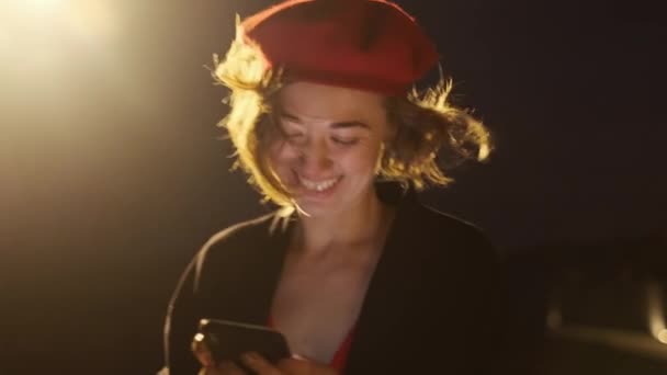 Crepúsculo. Jovem elegante em vermelho com telefone celular em suas mãos. Mulher vai para Cidade da Noite. — Vídeo de Stock
