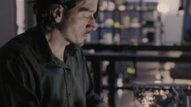 A focused man is working diligently with an advanced device in a spacious, modern workspace filled with shelves